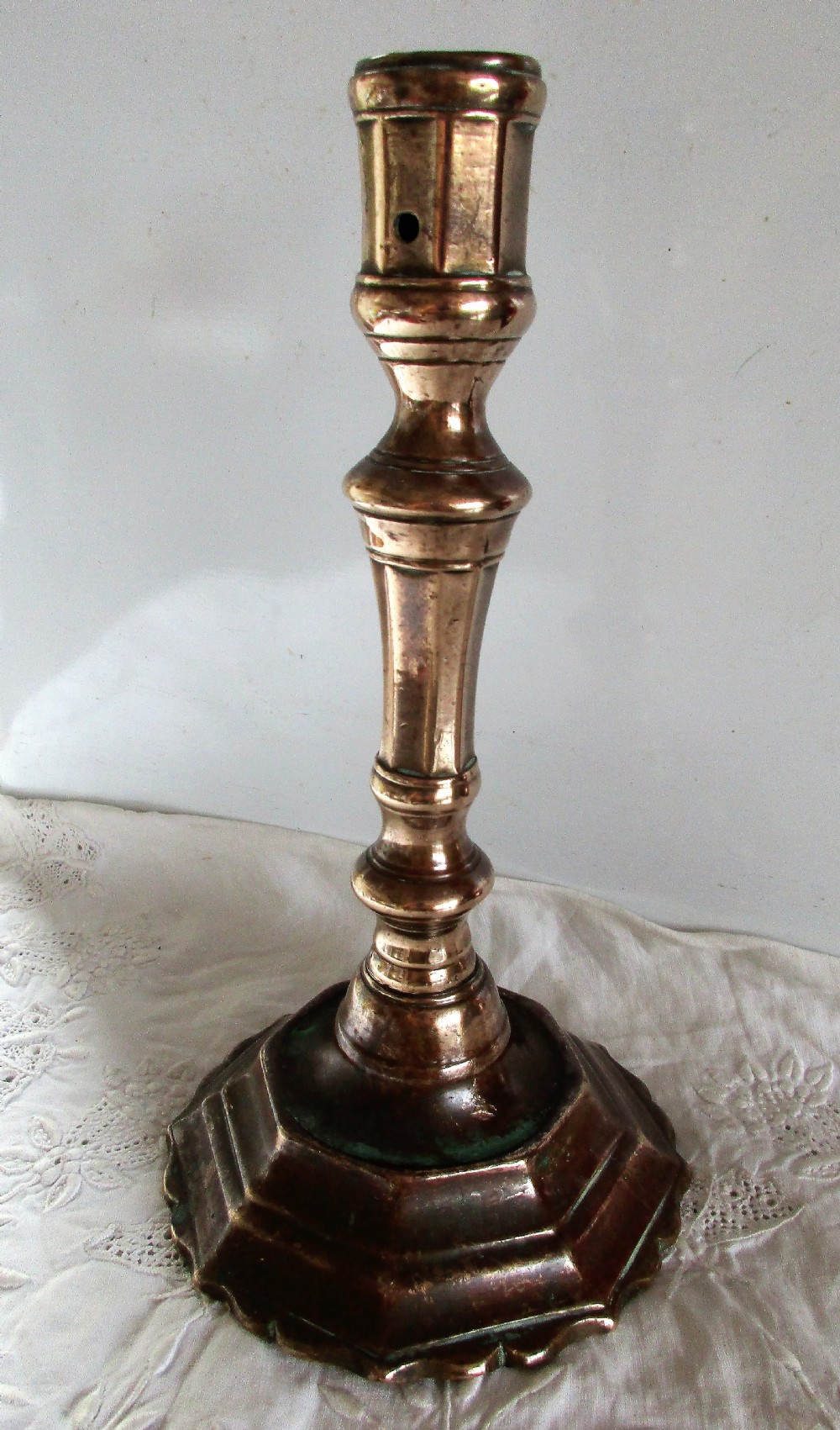 An antique cast bronze Georgian candlestick featuring a faceted baluster stem, socket with a wax ejector hole, and a scalloped octagonal stepped base.