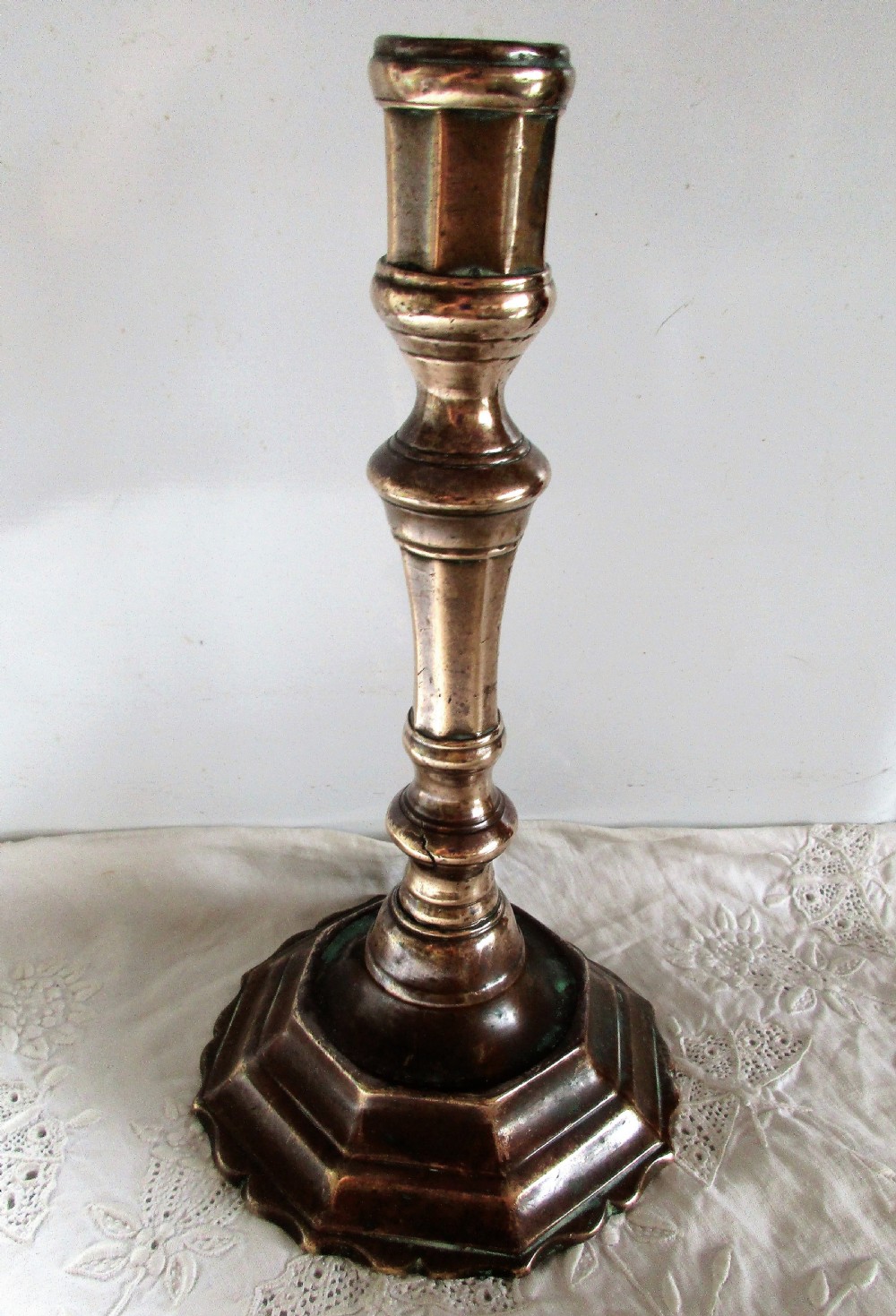 An antique cast bronze Georgian candlestick featuring a faceted baluster stem, socket with a wax ejector hole, and a scalloped octagonal stepped base. View II