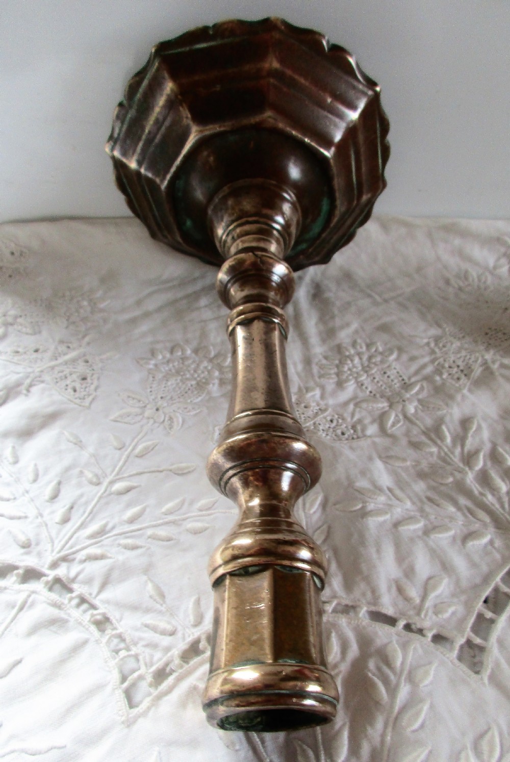 An antique cast bronze Georgian candlestick featuring a faceted baluster stem, socket with a wax ejector hole, and a scalloped octagonal stepped base. View III