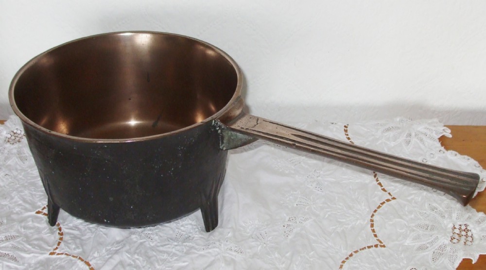 An antique Georgian cast bronze posnet skillet featuring three short legs, a long grooved handle, and a polished interior.