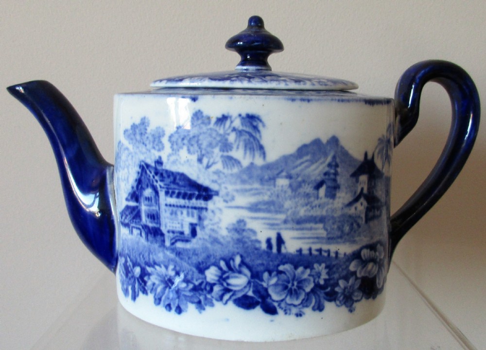 A Victorian blue and white transferware teapot decorated with an alpine landscape scene, cobalt blue spout, lid finial, and curved handle.