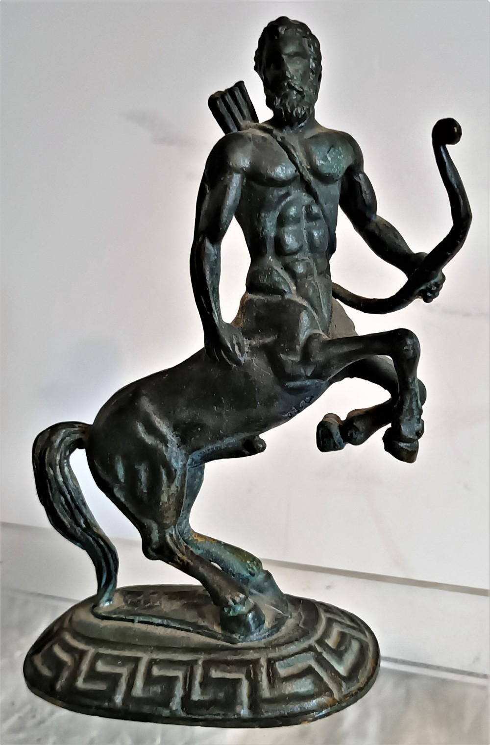 A dark patinated bronze figurine depicting a rearing centaur archer holding a bow on an oval base with a Greek key pattern.