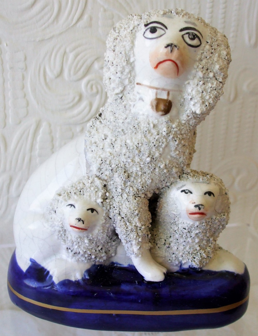 An antique Victorian Staffordshire ceramic figure group featuring a mother poodle with two smaller puppies on a cobalt blue base with textured fleece details.
