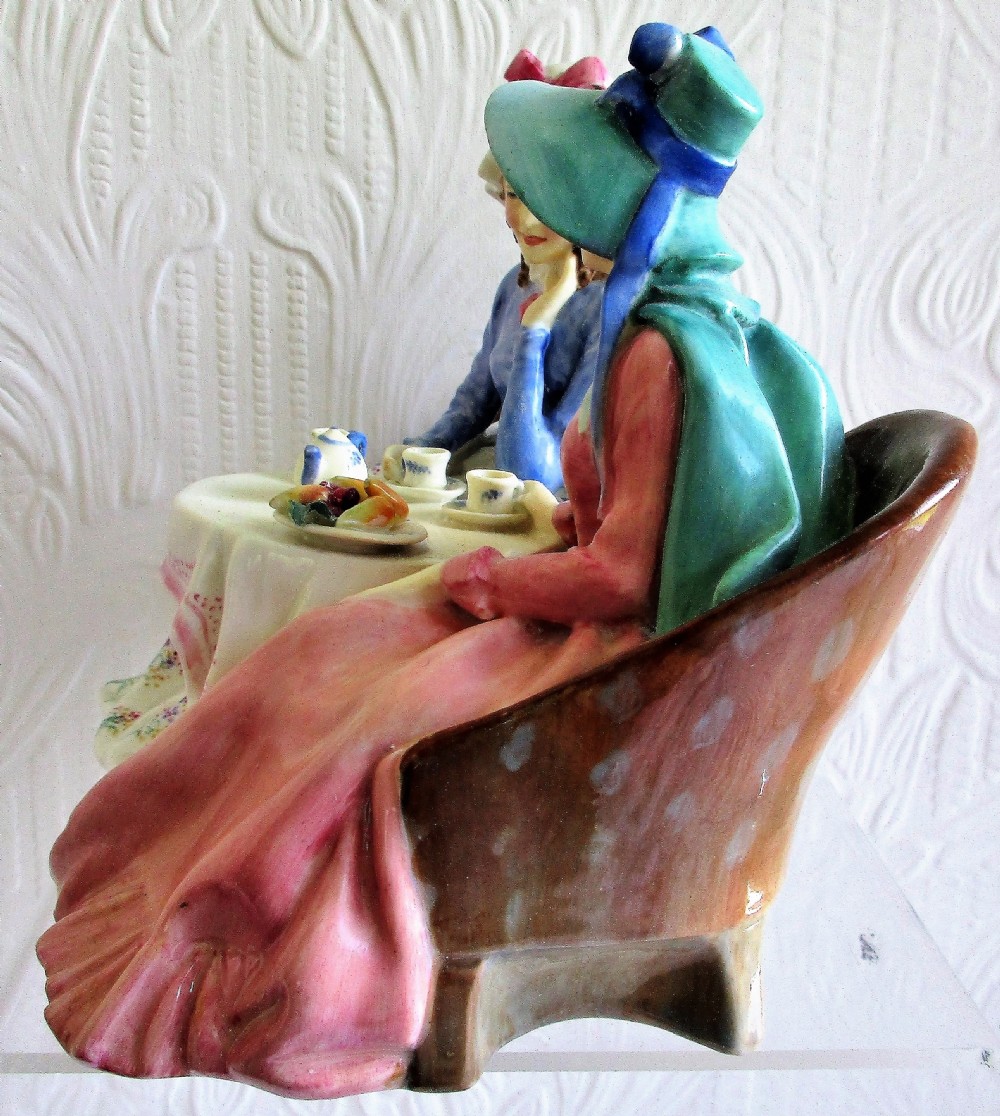 A glazed Royal Doulton porcelain figurine depicting two women in 19th-century attire seated at a tea table. View II