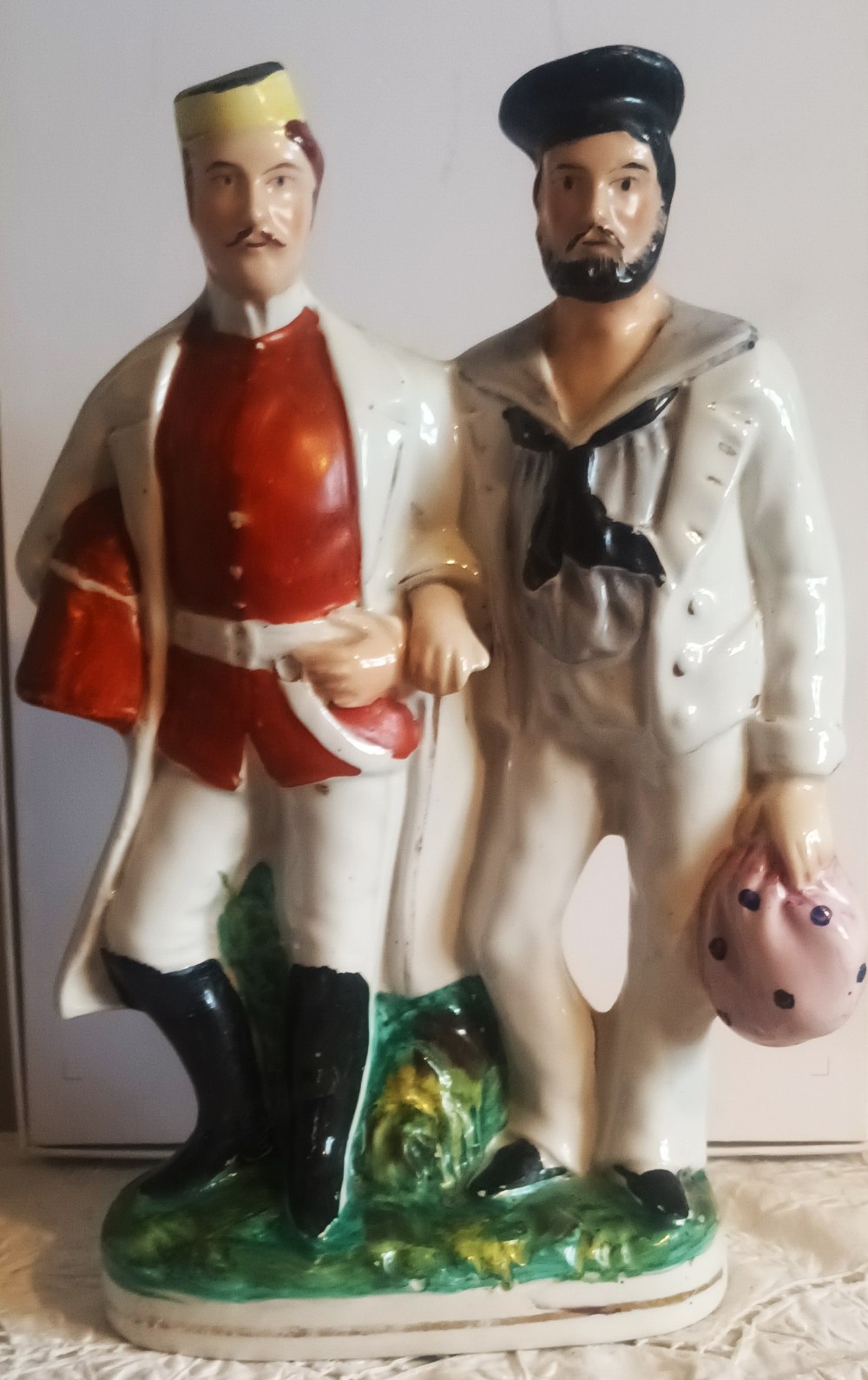 Victorian Staffordshire pottery flatback figure depicting a soldier in a red tunic and a sailor in a white uniform standing together on a moulded green base.