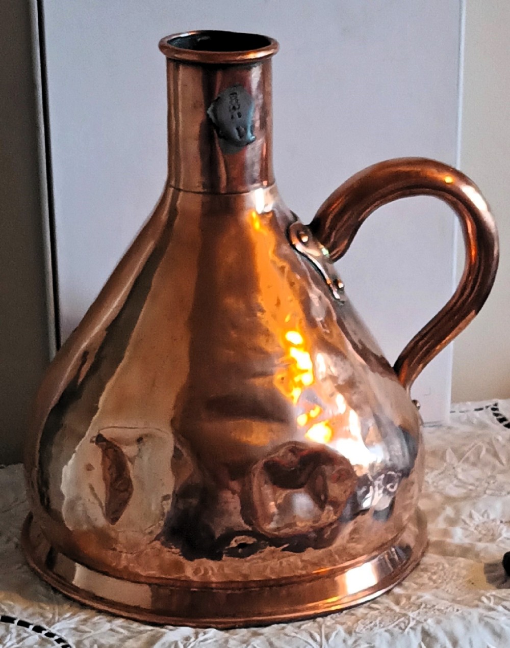A Georgian copper one-gallon haystack measure with a conical body, narrow neck, broad strap handle, and a lead verification seal.