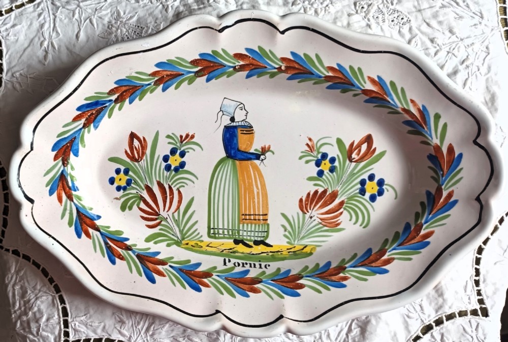 An oval cream ceramic faience dish with a scalloped edge, hand-painted with a Breton figure, floral motifs, and the name Pornic.