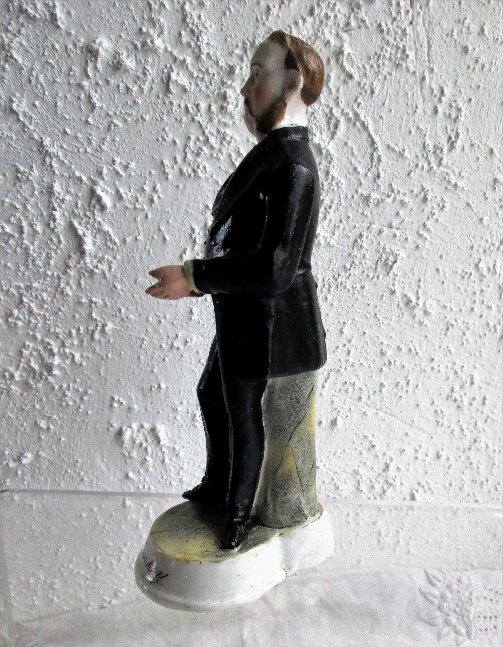 An antique Victorian porcelain figurine depicting a standing man in a black frock coat and bow tie on a round white base inscribed Mr Sankey. View II