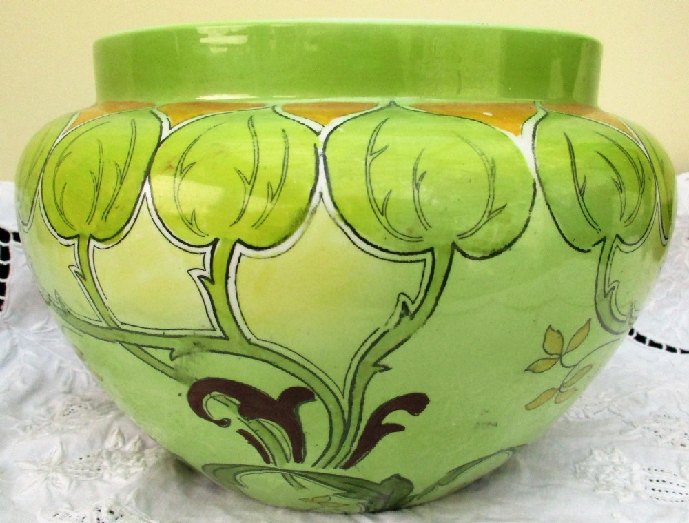 An antique Art Nouveau glazed ceramic jardiniere featuring a vibrant green ground decorated with stylized botanical leaf motifs and yellow accents.