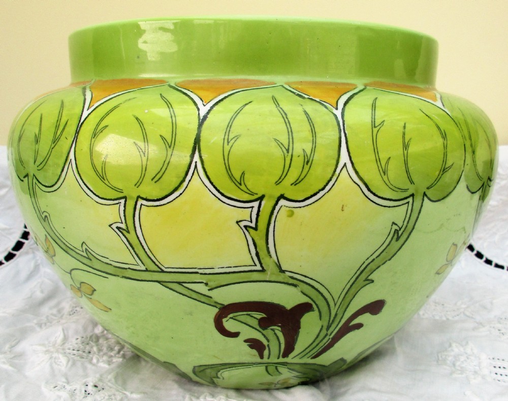An antique Art Nouveau glazed ceramic jardiniere featuring a vibrant green ground decorated with stylized botanical leaf motifs and yellow accents. View II