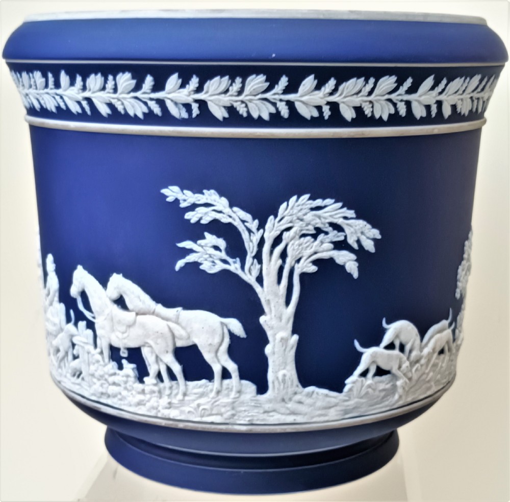A cobalt blue ceramic jasperware jardiniere decorated with white raised relief scenes of a traditional hunt surrounded by foliage and a leaf band along the rim. View III