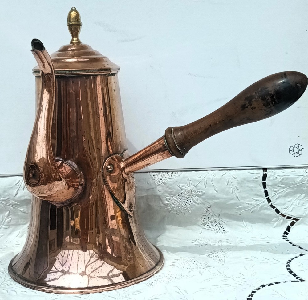 An antique Georgian copper coffee pot featuring a tapered body, a curved gooseneck spout, a top brass finial, and a turned wooden side handle.