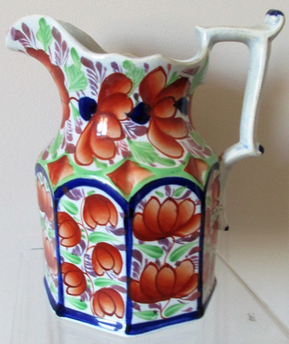 An antique octagonal earthenware jug featuring hand-painted orange floral motifs, cobalt blue borders, green foliage, and a molded handle.