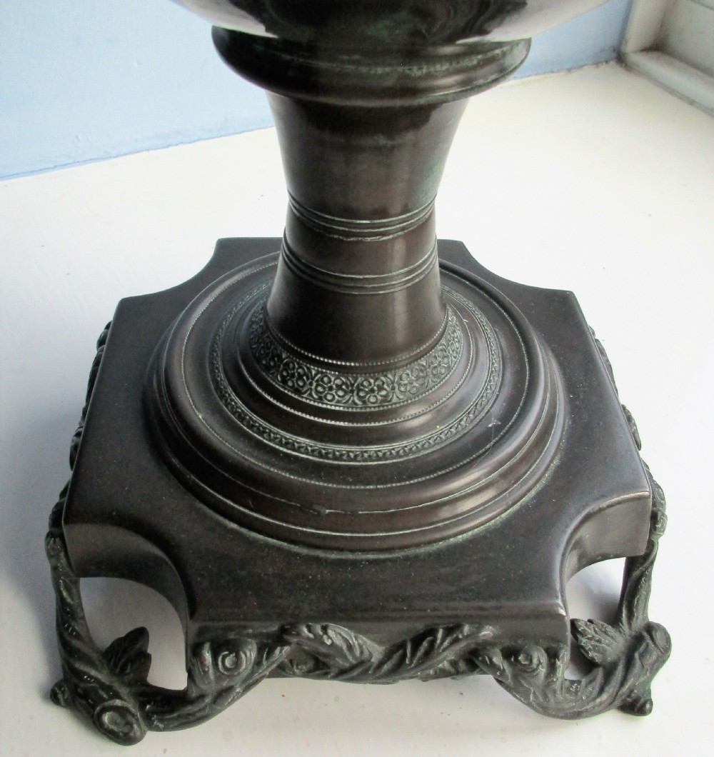 A dark patinated metal Victorian tea urn featuring a bulbous body, twin side handles, a front spigot with a white handle, and a pointed lid. View VII