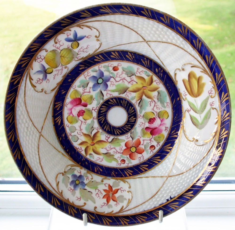 A circular Georgian New Hall porcelain dish featuring a cobalt blue gilded border and hand-painted polychrome floral motifs on a white moulded ground.