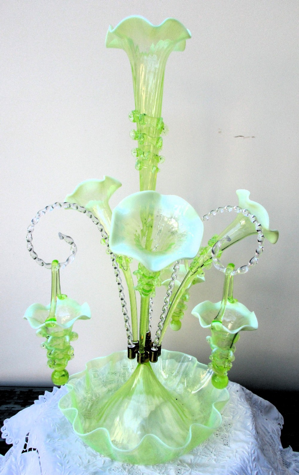 An antique Victorian pale green glass epergne with a tall central trumpet flue, surrounding smaller flues, hanging glass baskets, and a crimped ruffled bowl base.