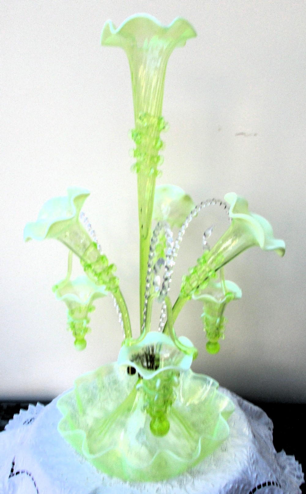An antique Victorian pale green glass epergne with a tall central trumpet flue, surrounding smaller flues, hanging glass baskets, and a crimped ruffled bowl base. View II
