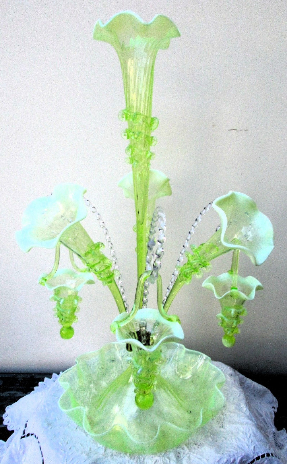 An antique Victorian pale green glass epergne with a tall central trumpet flue, surrounding smaller flues, hanging glass baskets, and a crimped ruffled bowl base. View III