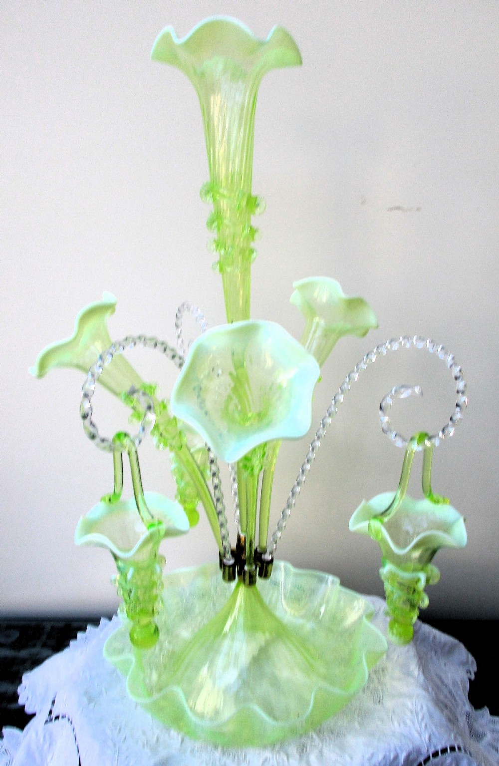 An antique Victorian pale green glass epergne with a tall central trumpet flue, surrounding smaller flues, hanging glass baskets, and a crimped ruffled bowl base. View IV