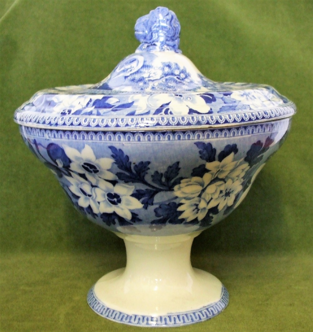 An antique blue and white transfer-printed earthenware tureen featuring a pedestal base, floral patterns, and a fitted lid with a molded animal finial.
