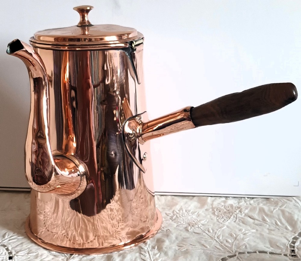A Georgian copper coffee pot featuring a tapered body, a curved spout, a hinged lid with finial, and a turned wooden side handle.
