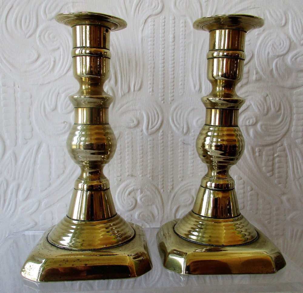 A pair of turned Victorian brass candlesticks featuring baluster stems and square bases.