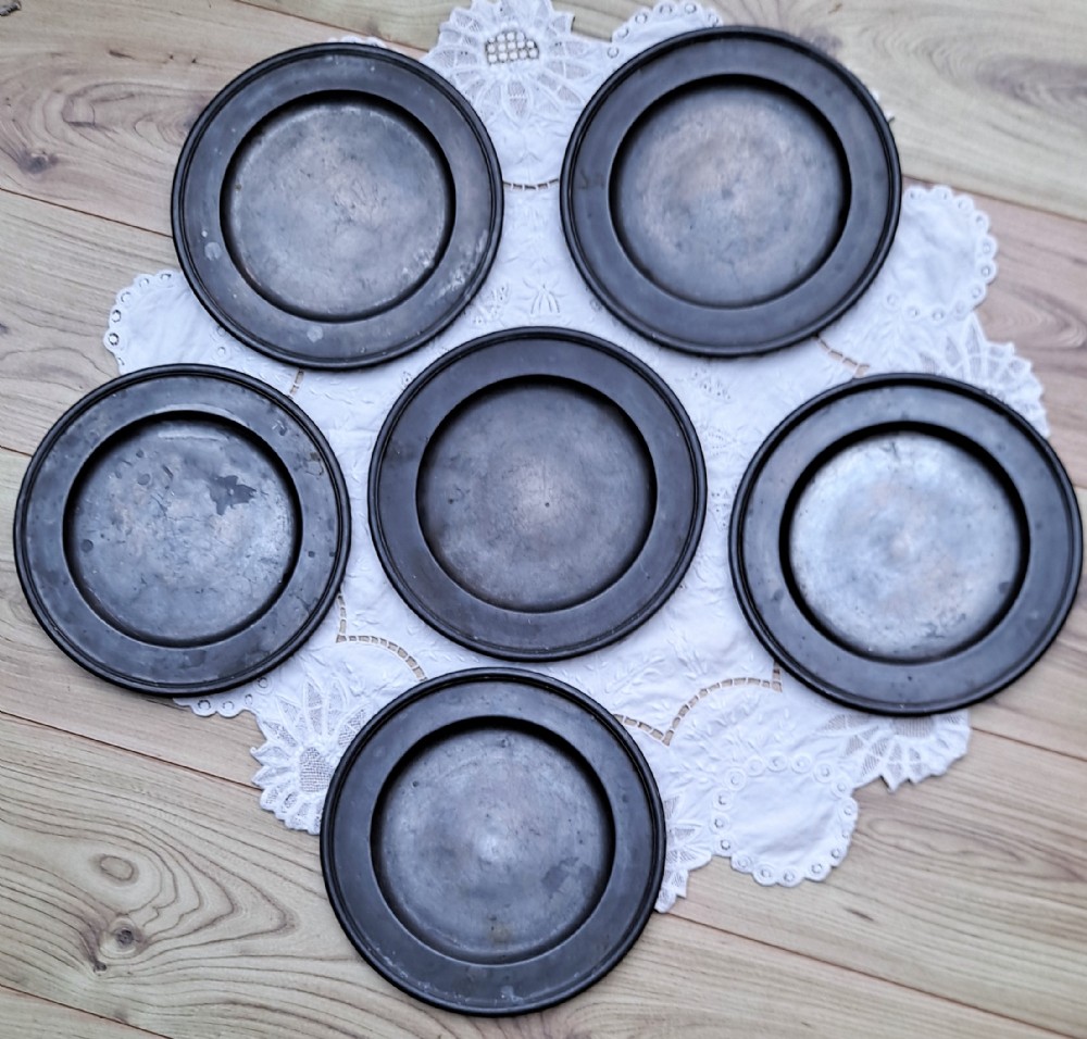 A set of six circular antique pewter plates displaying aged dark grey patination and flat rims.