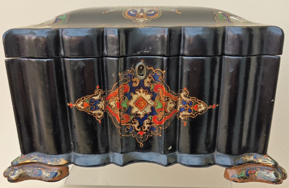 A Victorian black lacquered papier-mache tea caddy featuring a lobed serpentine body, central polychrome arabesque motif, and brass escutcheon on gilded feet.