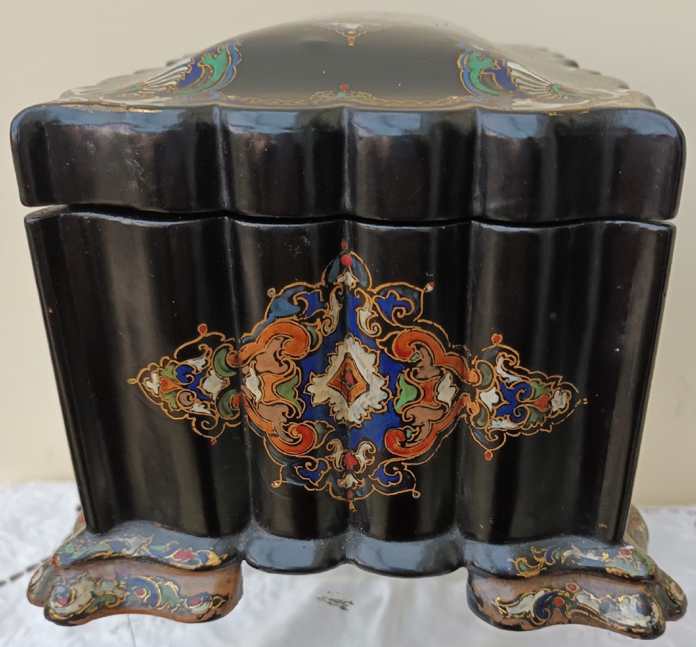 A Victorian black lacquered papier-mache tea caddy featuring a lobed serpentine body, central polychrome arabesque motif, and brass escutcheon on gilded feet. View IV