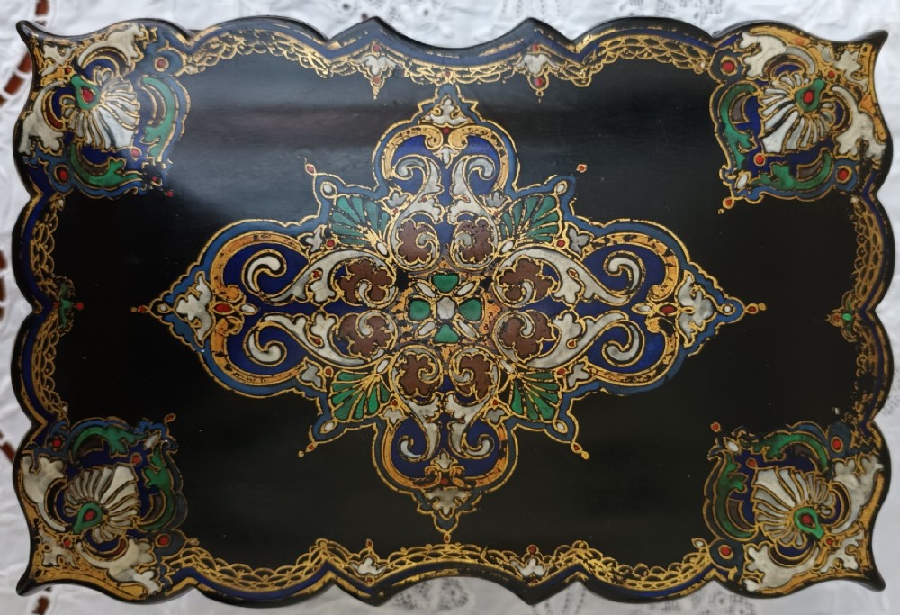 A Victorian black lacquered papier-mache tea caddy featuring a lobed serpentine body, central polychrome arabesque motif, and brass escutcheon on gilded feet. View V