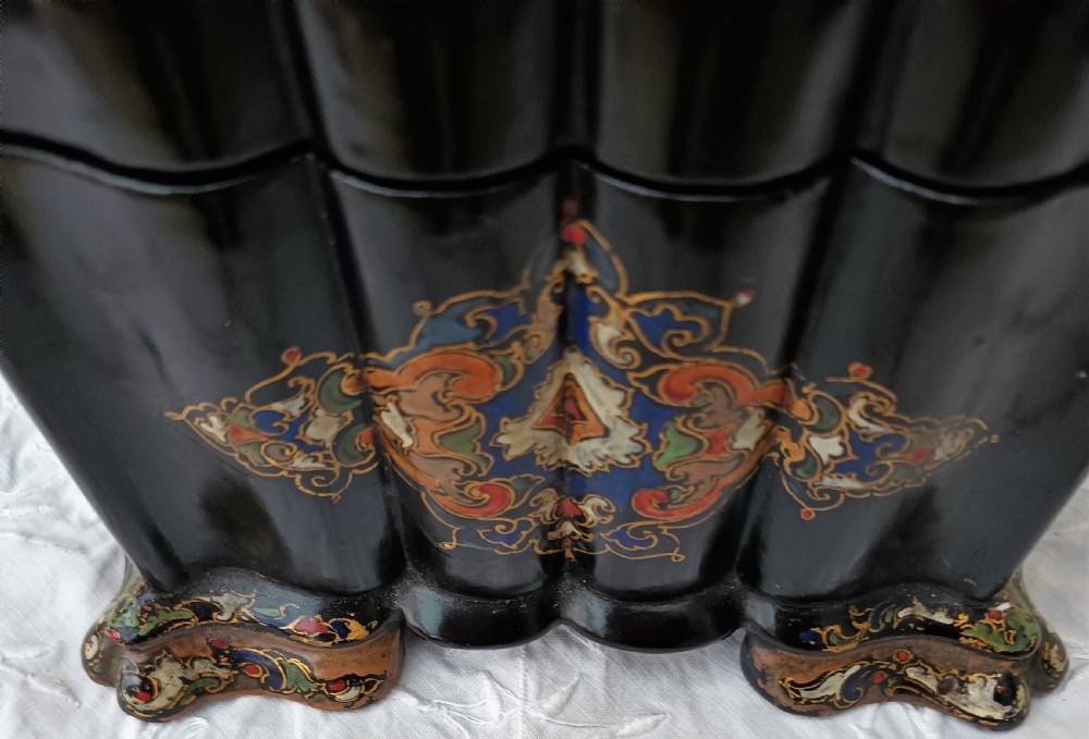 A Victorian black lacquered papier-mache tea caddy featuring a lobed serpentine body, central polychrome arabesque motif, and brass escutcheon on gilded feet. View VI