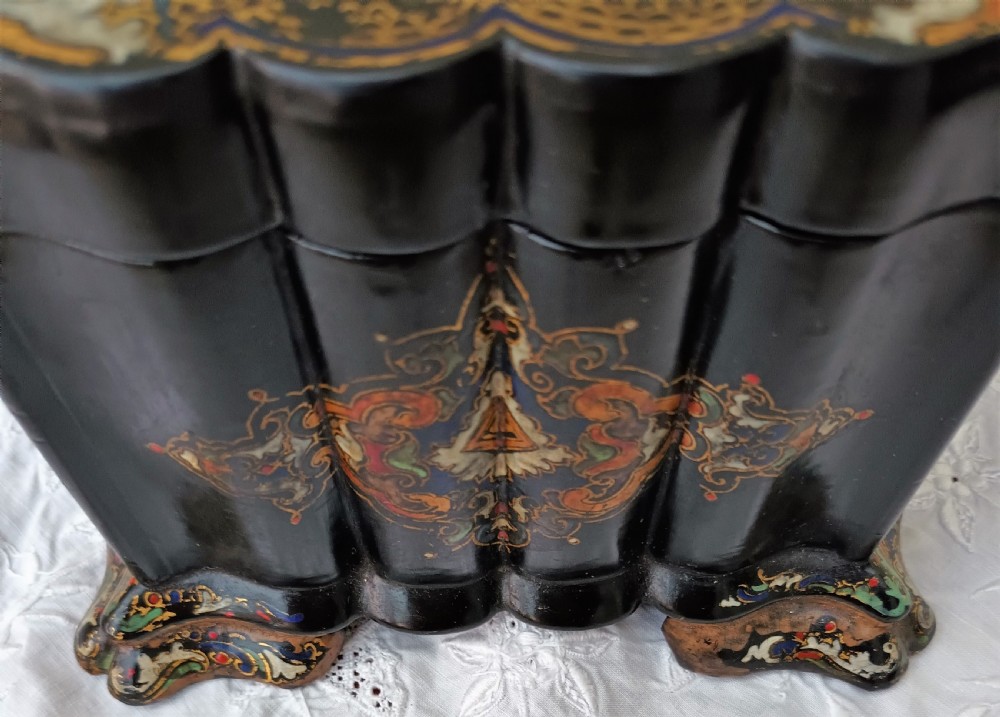 A Victorian black lacquered papier-mache tea caddy featuring a lobed serpentine body, central polychrome arabesque motif, and brass escutcheon on gilded feet. View VII
