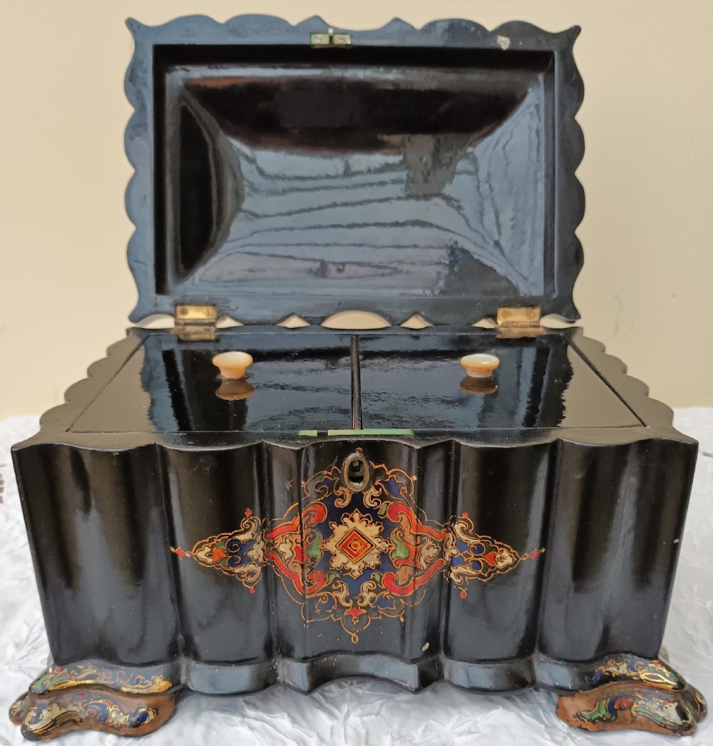A Victorian black lacquered papier-mache tea caddy featuring a lobed serpentine body, central polychrome arabesque motif, and brass escutcheon on gilded feet. View IX