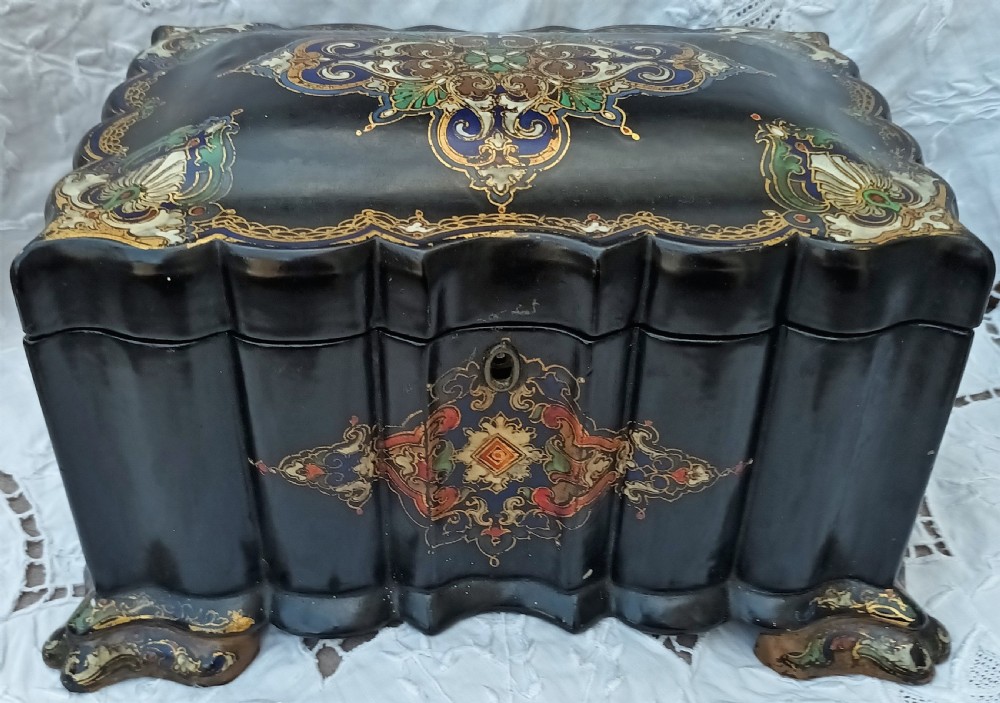 A Victorian black lacquered papier-mache tea caddy featuring a lobed serpentine body, central polychrome arabesque motif, and brass escutcheon on gilded feet. View XVI