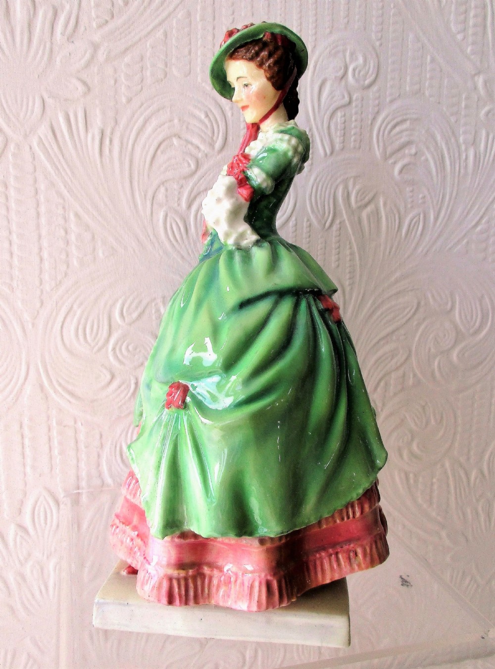 A vintage Royal Doulton porcelain figurine titled Kate Hardcastle depicting a woman in an 18th-century style green overskirt and pink ruffled dress. View II