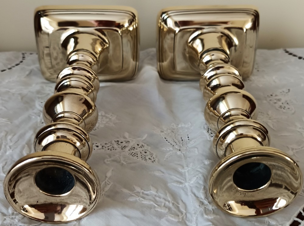 A pair of polished Georgian brass candlesticks featuring turned knopped stems on stepped square bases. View V