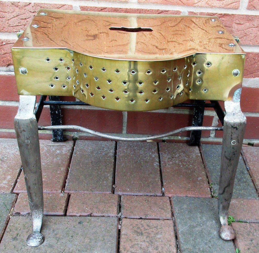 An antique Georgian brass and steel fireplace footman stand with a pierced lattice apron, cabriole front legs, and top carrying handle.