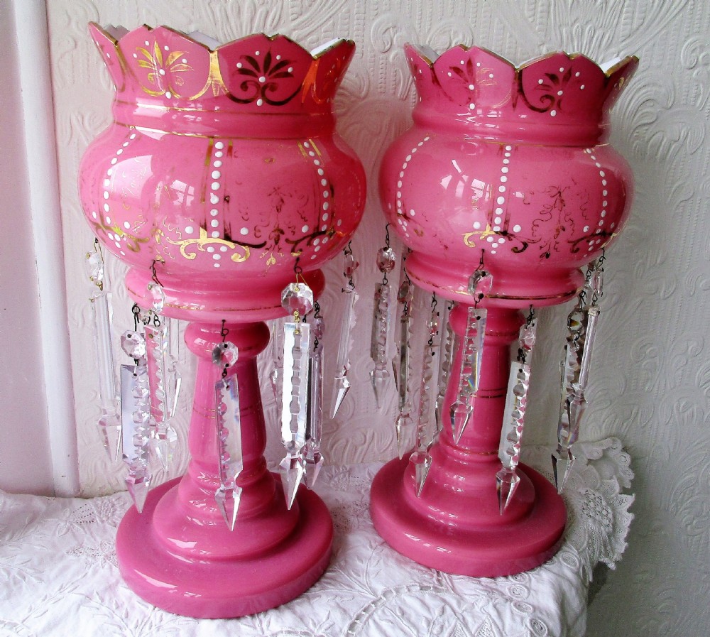 A pair of Victorian pink glass lustres decorated with gilded scrolling, enamel dots, scalloped rims, and suspended clear cut-glass prisms.