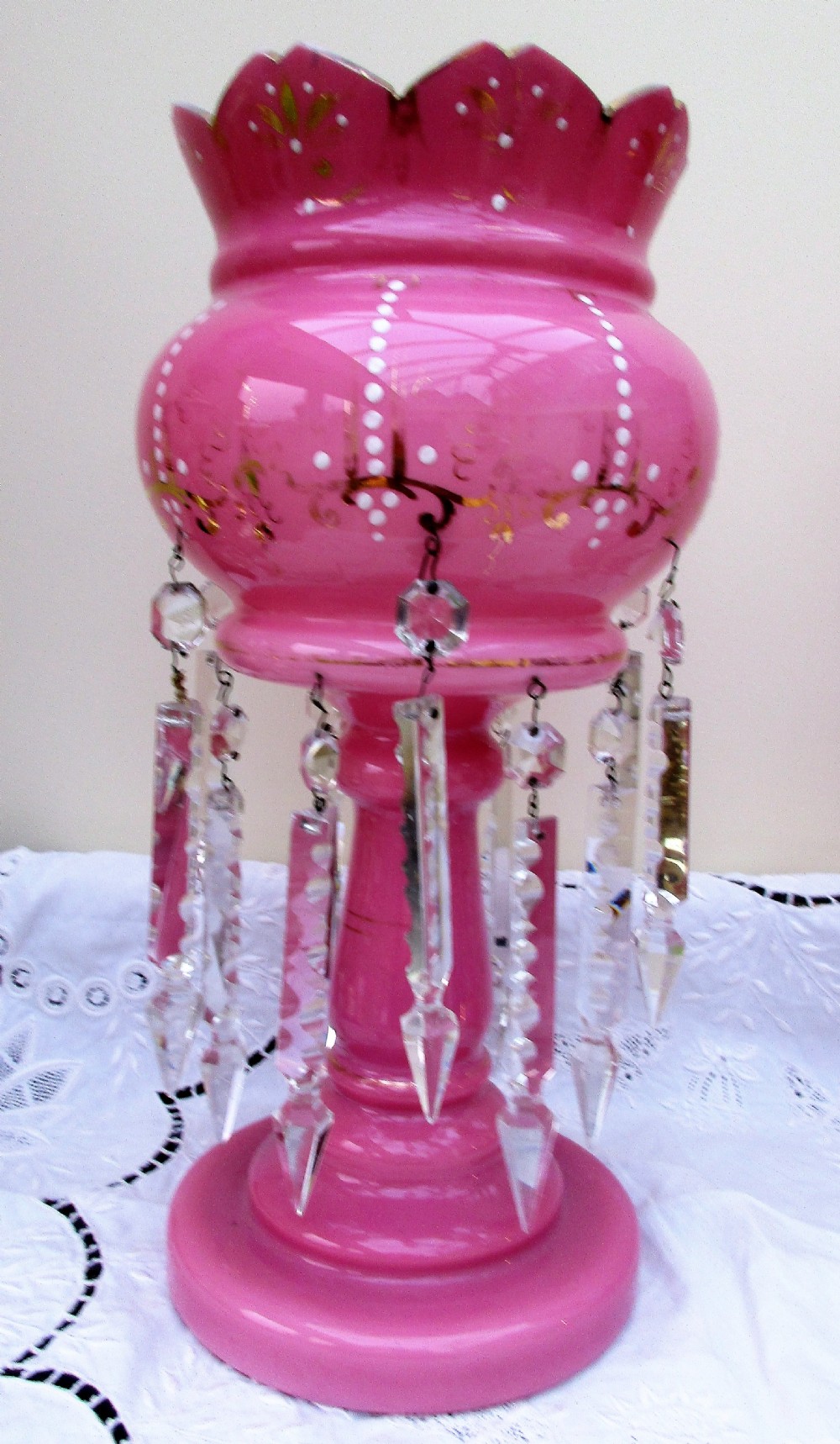 A pair of Victorian pink glass lustres decorated with gilded scrolling, enamel dots, scalloped rims, and suspended clear cut-glass prisms. View II