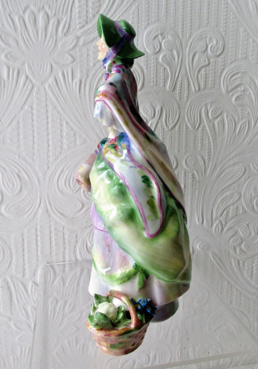 A hand-painted Royal Doulton bone china figurine depicting a female figure in a green bonnet and floral patterned cloak. View II