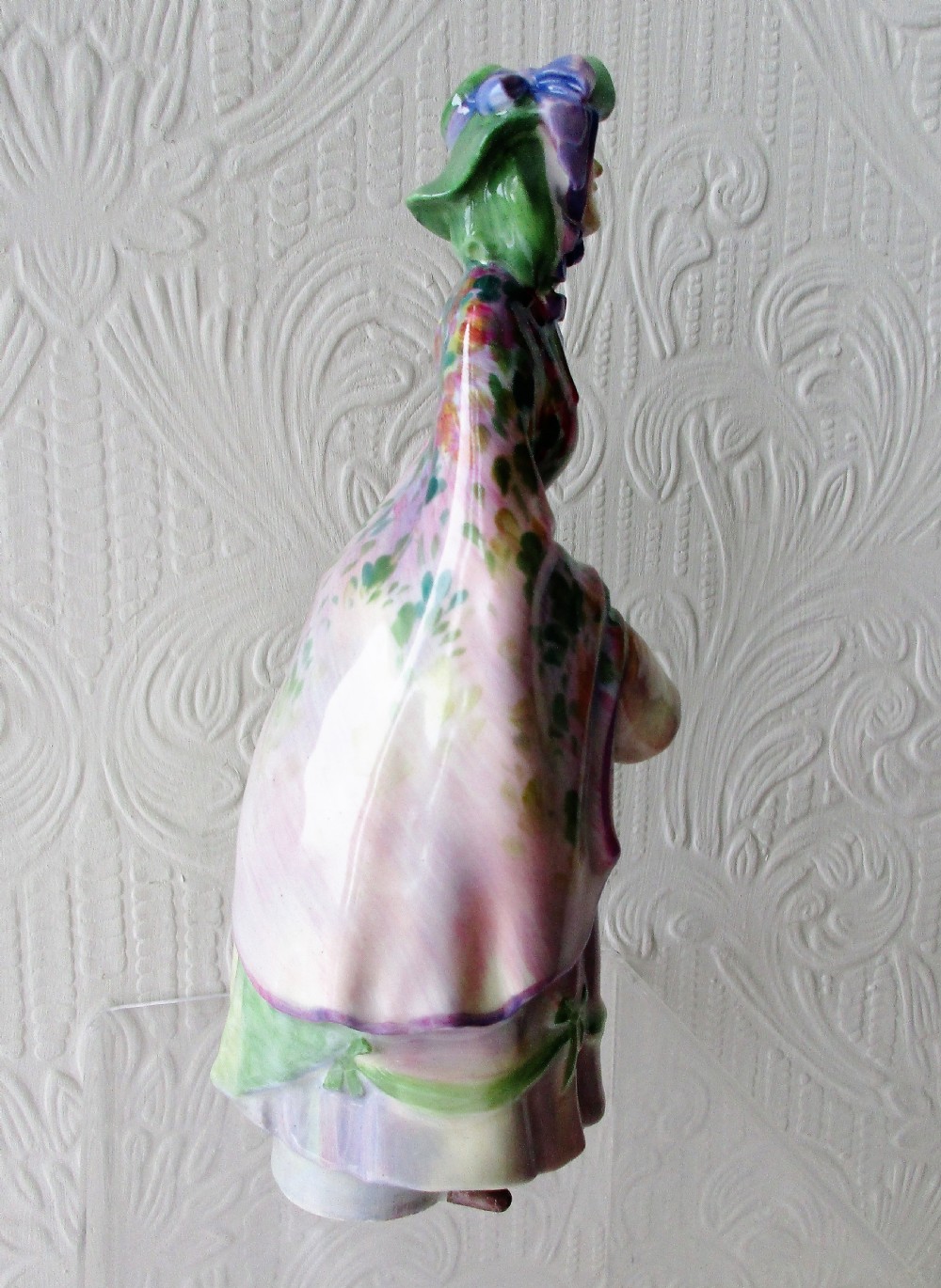 A hand-painted Royal Doulton bone china figurine depicting a female figure in a green bonnet and floral patterned cloak. View IV
