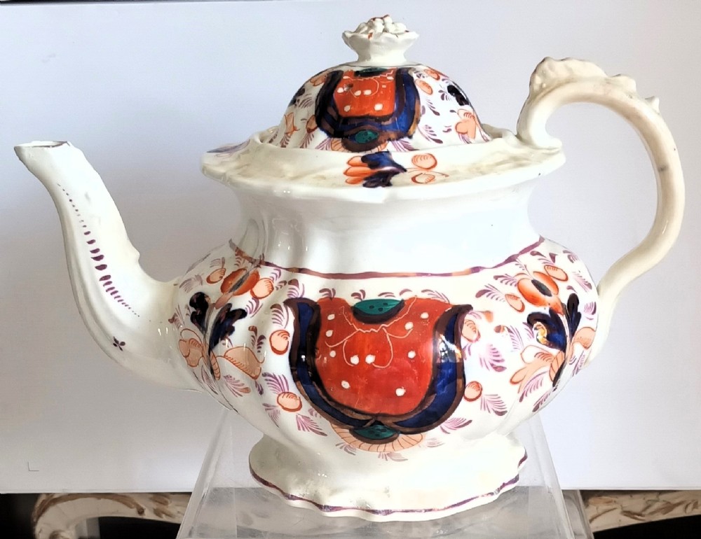 An antique Georgian earthenware teapot featuring a hexagonal fluted shape, hand-painted rust red and cobalt blue motifs with lustre highlights, a curved spout, and a finial lid.