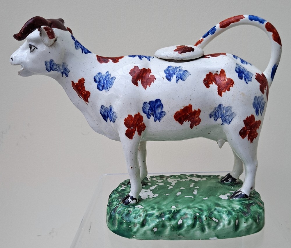 A Georgian earthenware cow creamer decorated with blue and red hand-painted spots on a green moulded base.