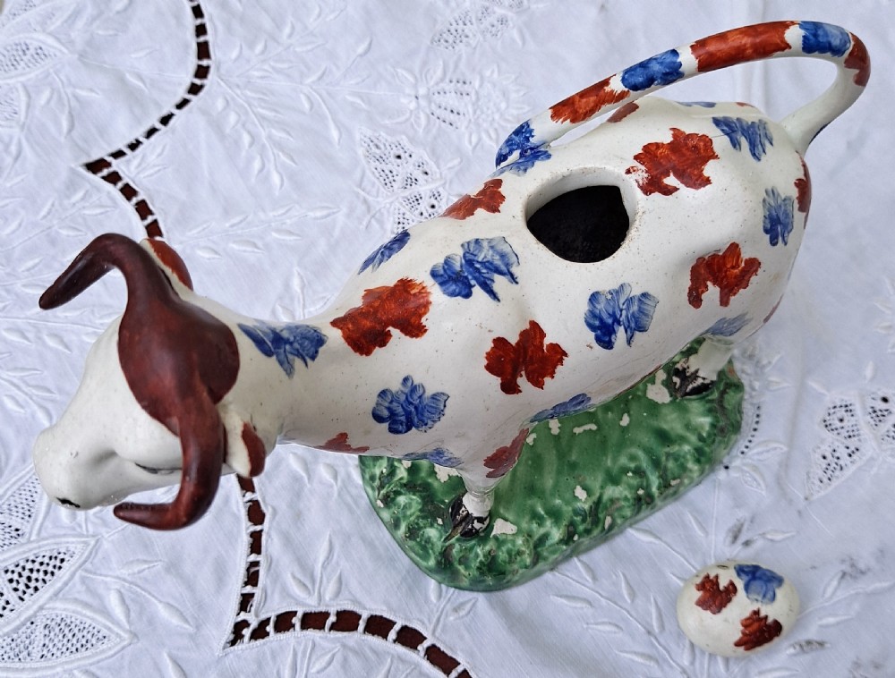 A Georgian earthenware cow creamer decorated with blue and red hand-painted spots on a green moulded base. View V