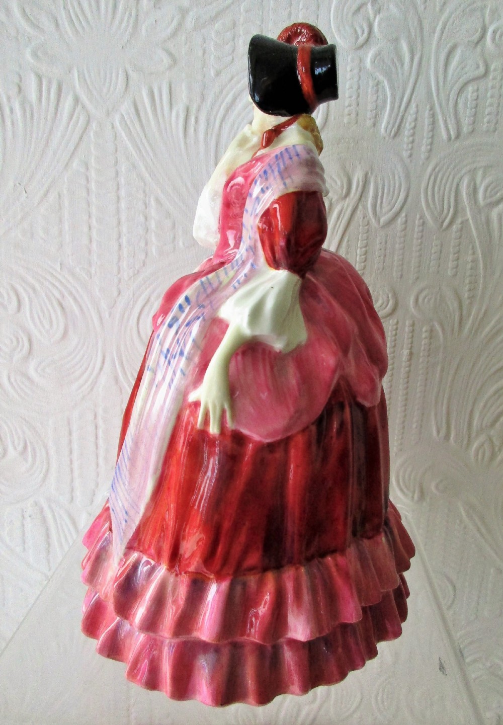 A Royal Doulton porcelain figurine titled Quality Street featuring a woman in a tiered magenta dress, bonnet, and patterned sash resting her hand on her chin. View II