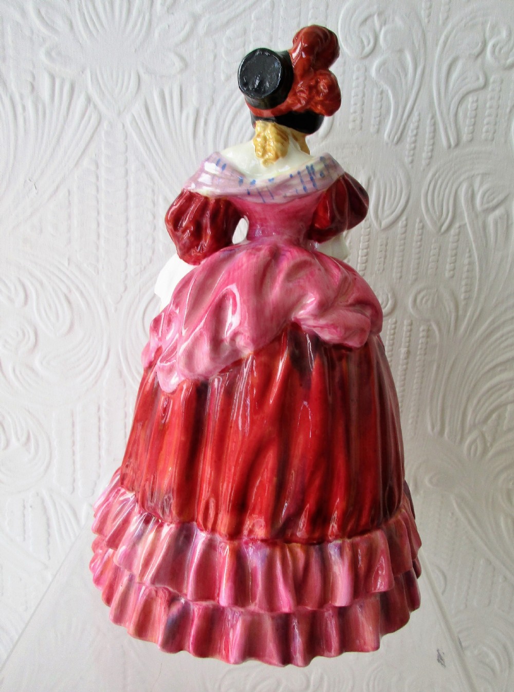 A Royal Doulton porcelain figurine titled Quality Street featuring a woman in a tiered magenta dress, bonnet, and patterned sash resting her hand on her chin. View III