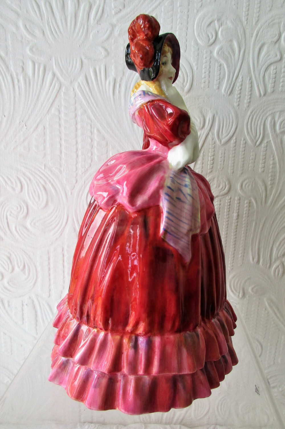A Royal Doulton porcelain figurine titled Quality Street featuring a woman in a tiered magenta dress, bonnet, and patterned sash resting her hand on her chin. View IV