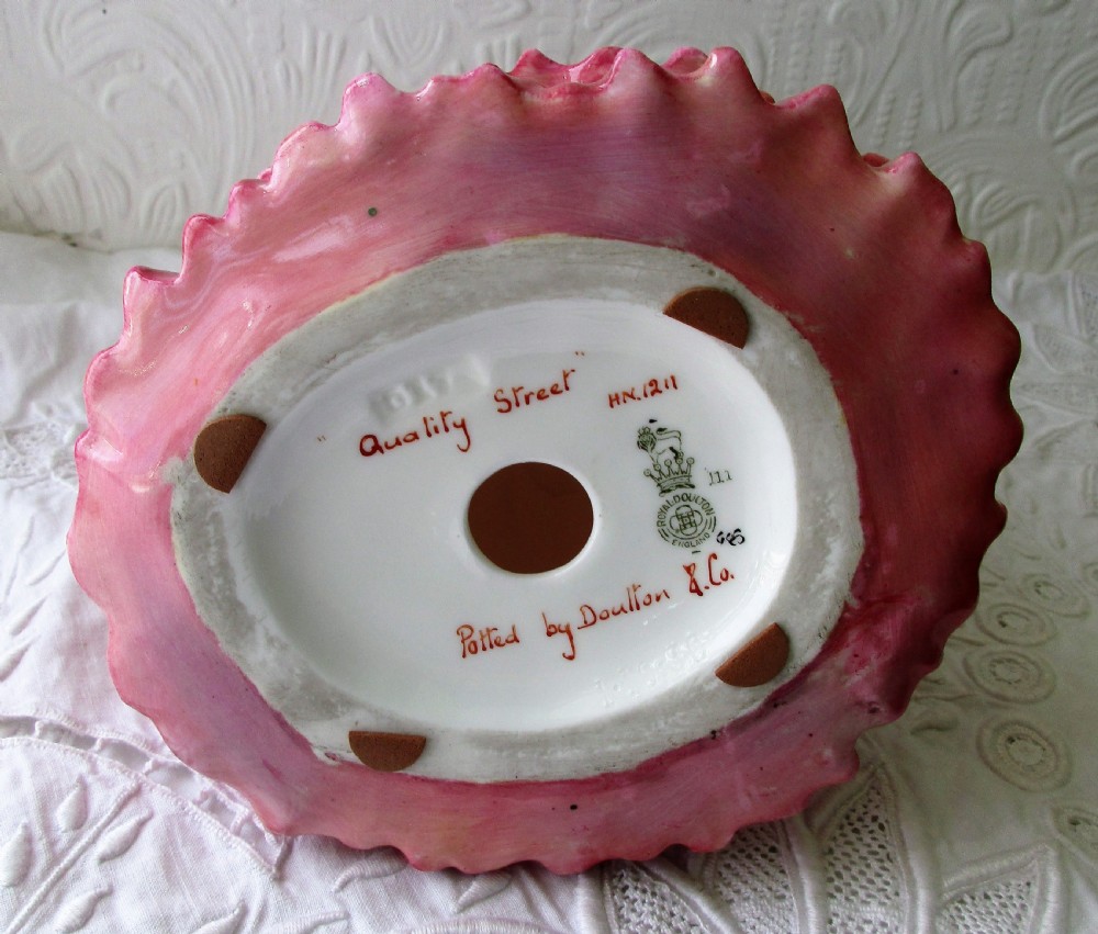 A Royal Doulton porcelain figurine titled Quality Street featuring a woman in a tiered magenta dress, bonnet, and patterned sash resting her hand on her chin. View V