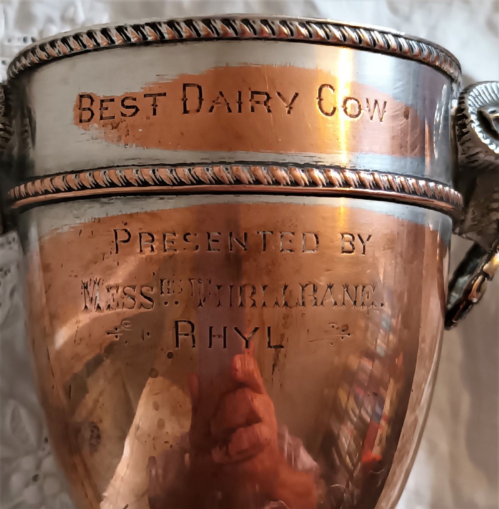 A miniature Georgian Old Sheffield Plate urn featuring a fitted lid with a finial, square base, engraved inscription, and rams head side handles. View VI