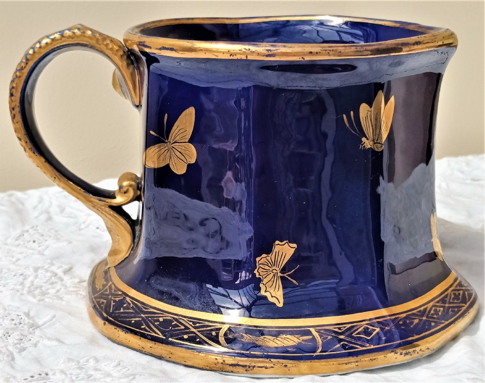 An antique cobalt blue ironstone mug featuring flared sides, a gilded scroll handle, and intricate gold floral motifs with a geometric border. View III